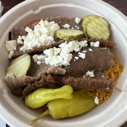 Gyro plate over rice with pickles, Peppercini and feta . Hummus, red cabbage and tomatoes are underneath.