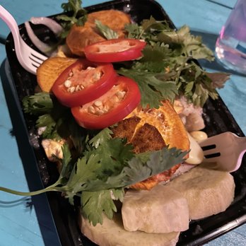 Ceviche7 - Ceviche de Pescado - A serving of ceviche garnished with tomato slices, cilantro, and fried plantains on a black tray, with a fork and a water glass nearby. - Peruvian Near Me - Austin, Texas
