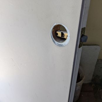 Cache Lock & Key - Second door - A door with a circular cutout where a handle or lock mechanism is missing, exposing internal hardware and a latch. The door appears to be part of an interior space, with visible hinges and a partially visible toilet or fixture behind it. The surface of the door is plain and light-colored, and the surrounding area shows signs of wear or construction. - Keys & Locksmiths Near Me - Logan, Utah