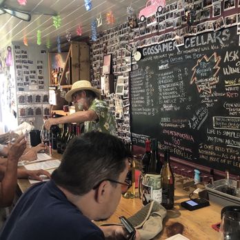 Gossamer Cellars - Tasting room! - People are seated at a bar in Gossamer Cellars, a boutique winery in Murphys, CA, with a chalkboard menu and photo wall behind them. - Wineries Near Me - Murphys, California