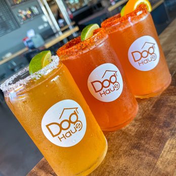 Dog Haus - Three handcrafted Dog Haus cocktails on a wooden table, including a salted-rim drink and michelada-style glasses with lime, h... - American Near Me - Waco, Texas
