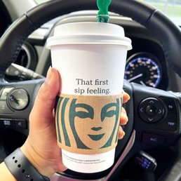 a hand holding a starbucks cup in a car