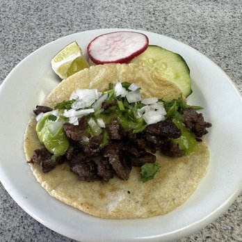 Plaza Teontepec - carne asada taco - A carne asada taco on a corn tortilla is topped with chopped onions and cilantro. The plate includes slices of cucumber, radish, and a lime wedge, all placed on a gray surface. The presentation highlights traditional Mexican flavors and fresh ingredients. - Tacos Near Me - Washington, DC, District of Columbia