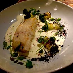 PIL-PIL MARKET FISH - A dish with a piece of white fish, garnished with microgreens, roasted vegetables, and drizzled with sauce, served on a white plate.