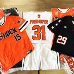 Custom Trophy / Active Edge - Several baseball jerseys in orange, white, and black with team names and numbers are laid out on a surface.
