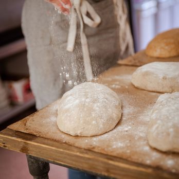 Lucky Penny Bread - a person sprinkling flour on a loaf of bread - Bakeries Near Me - San Rafael, California Lucky Penny Bread - a person sprinkling flour on a loaf of bread - Bakeries Near Me - San Rafael, California