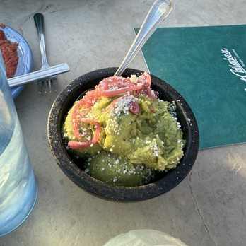 Aunt Chilada's - Guacamole - A black bowl contains guacamole topped with crumbled cheese and pink pickled onions, placed on a table at a restaurant. - Mexican Near Me - Tempe, Arizona