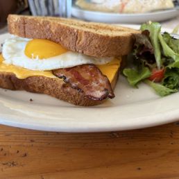 Breakfast sandwich with bacon as the protein sunny side up greens on the side