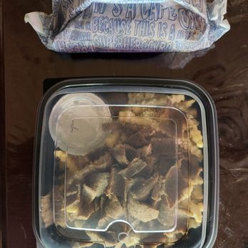 Gyro Shack - Great packaging. - A square plastic takeout container with a clear lid contains cooked beef strips and mashed potatoes. The container is on a dark wooden table. A small, round container of sauce is inside the lid, and a paper bag with blue text is positioned above the container. - Greek Near Me - Albuquerque, New Mexico