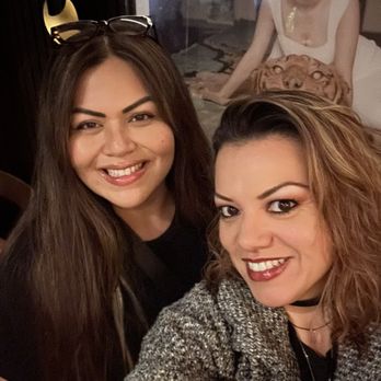The Corner Pub - Happy ladies - Two women are smiling and taking a selfie inside a bar or restaurant, with a poster of a woman in the background. The setting appears casual and social. - Dive Bars Near Me - Boston, Massachusetts