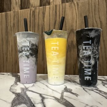 Tea Time - Black Sesame Taro Blend A2. Mango Sago Black Sesame Oat Milk - Three bubble tea drinks with black, yellow, and purple colors are placed on a marble table in front of a wooden wall. - Coffee & Tea Near Me - Albuquerque, New Mexico