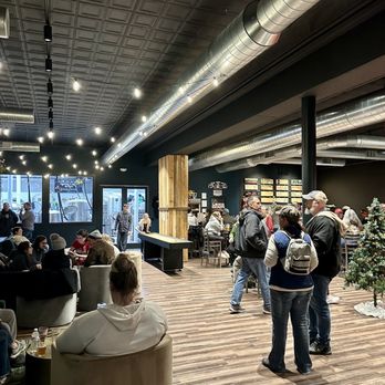 Darkroom Brewing - Inside - A brewery interior with a dark ceiling, exposed ductwork, and wooden flooring. Customers are seated and standing, enjoying drinks, with a Christmas tree in the corner. - Breweries Near Me - Geneva, Ohio