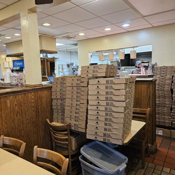 Frank's at Brambleton - A group of pizza boxes willed up on one of the tables in front of the kitchen that can be seen in the background. - Pizza Near Me - Roanoke, Virginia