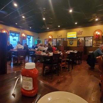 Oscar's Alehouse - My rueben and French fries were  perfect  . Service was a little slow however they were busy. Prices were also reasonable. - A restaurant interior with multiple tables and diners, featuring a dark ceiling, warm lighting, and framed posters on the walls. A condiment bottle is visible in the foreground. - New American Near Me - Eldersburg, Maryland