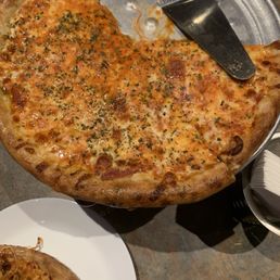 Cheese Pizza - A large slice of cheese pizza with herbs on top, served on a metal tray with a pizza cutter, at a restaurant.