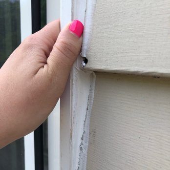 Girls 'n' Tools - Siding cut and filled with a ridiculous amount of caulking - A person with pink-painted nails is holding a damaged section of siding or trim near a window on a house exterior. - General Contractors Near Me - Danielson, Connecticut