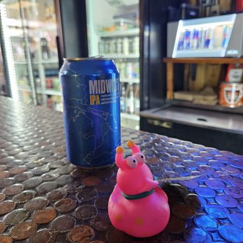 Mike's Grill - A pink rubber snail toy with googly eyes and a can of Midwest IPA are placed on a textured copper bar counter in a casual setting. - Dive Bars Near Me - Columbus, Ohio