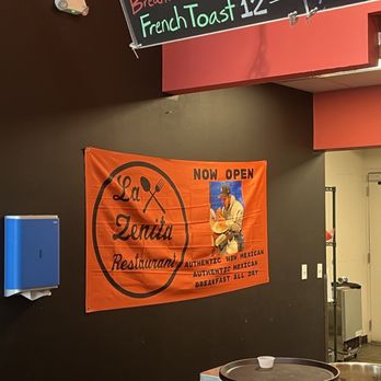 La Zenita - An orange fabric banner for La Zenita Restaurant, a Mexican eatery, is hung on a dark wall, featuring the restaurant's name, a graphic of a spoon and fork, and a photo of a man eating. - Mexican Near Me - Albuquerque, New Mexico