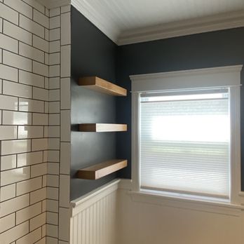 Victor's Finish Work - Custom shelving, beadboard ceiling, trim work - Three wooden shelves are installed on a dark blue wall next to a window with white trim and blinds, in a room with white beadboard paneling. - Refinishing Services Near Me