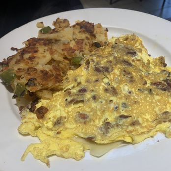Cantina 35  - Create Your Omelette - The image shows a white plate holding a cooked omelette containing pieces of meat and vegetables, with a slightly browned exterior. Next to the omelette is a serving of potato hash mixed with diced green peppers and other vegetables. The dish appears to be served in a casual dining setting, with the focus on the food presentation. - Mexican Near Me - Queens, New York