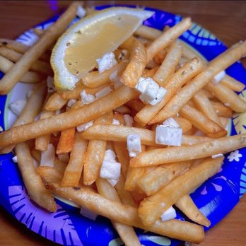 Freskos - Hamden - Greek Fries - A serving of French fries topped with crumbled feta cheese and garnished with a lemon wedge is presented on a colorful, patterned plate. The fries are golden and crispy, with the feta cheese adding a white, crumbly texture. The lemon wedge provides a citrus accent, and the plate features a vibrant blue and yellow design, suggesting a Greek or Mediterranean style of presentation. - Greek Near Me - Hamden, Connecticut
