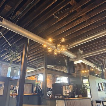 The Alchemist - A coffee shop interior featuring exposed wooden ceiling beams, metallic ductwork, and modern lighting fixtures, with seating and a counter area. - Coffee & Tea Near Me - Indianapolis, Indiana