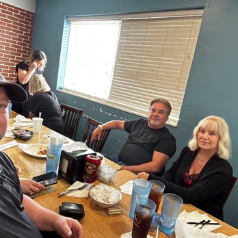 Ziggie's - Back room - Four people are seated at a wooden dining table in a restaurant with a blue wall and a window with blinds behind them. The table has drinks, food, napkins, and condiments. Two women and two men are visible, with one man taking a selfie. The setting appears casual, with some food remnants and personal items on the table. - New American Near Me - Springfield, Missouri