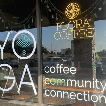 Flora Coffee - Flora Coffee's window displays neon signs with the business name and symbols, along with words like 'coffee' and 'community,' with reflections of parked cars outside. - Coffee & Tea Near Me - Austin, Texas