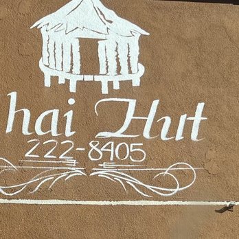 Thai Hut - Thai Food - Wall sign for Thai Hut restaurant featuring the restaurant's name, phone number, and a logo of a traditional Thai hut. The sign is painted in white on a beige wall, with decorative elements beneath the text. - Thai Near Me - Redding, California
