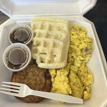 Cozy Corner - A takeout meal in a foam container includes scrambled eggs, a sausage patty, waffles, and two small cups of syrup. - Breakfast & Brunch Near Me - Brazil, Indiana