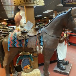 Horse - A large horse statue with a saddle and colorful blanket is displayed indoors, with store shelves and signage visible in the background.