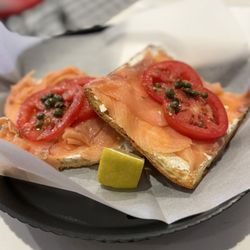 Smoked salmon toast with fresh tomatoes, capers, cream cheese, and a wedge of lemon