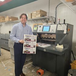 Minuteman Press - Jim showing off postcards in front of commercial cutter.