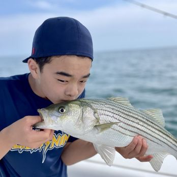 Blue Bandit Charters - Got to kiss the first catch. - A boy wearing a navy cap and shirt is holding a sizable fish on a boat, with the ocean and sky in the background. - Boat Charters Near Me