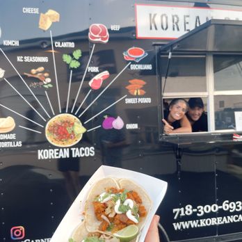Korean Carne - a hand holding a taco in front of a food truck - Caterers Near Me Korean Carne - a hand holding a taco in front of a food truck - Caterers Near Me