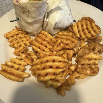 Cafe 20 - A white plate holds two wraps filled with ingredients such as lettuce, meat, and vegetables, with one wrap partially open to reveal the filling. Surrounding the wraps is a generous portion of golden-brown waffle fries. The background includes a gray countertop and a small container of dipping sauce. - American Near Me - Marengo, Illinois