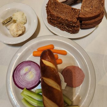 Chef Klaus' Bier Stube - Complimentary appetizers: different breads with various butter. Liver spread is served with the veggies and bread. - A plate contains a sausage, sliced onion, celery, and carrots, with bread and cake slices on separate plates, and butter with cheese on a small dish. - German Near Me - Frankfort, Illinois