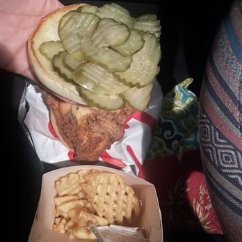 Chick-fil-A - A fish sandwich with pickles is held in a hand, with waffle fries and a dipping sauce in a small basket below, set inside a vehicle. - Fast Food Near Me - Worcester, Massachusetts