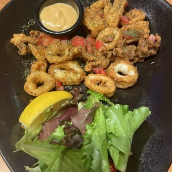 Lavender Grill - Calamari - Fried calamari rings and pieces with a side of mustard sauce, lemon wedge, and mixed greens salad on a black plate. - Steakhouses Near Me - Ottawa, Ontario