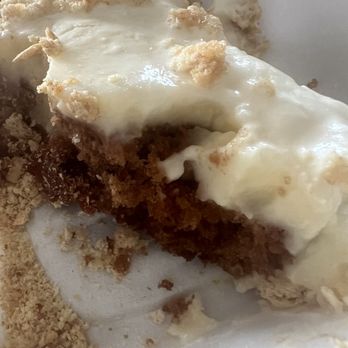 Texas Steele BBQ - Carrot Pudding Cake - A close-up of a carrot pudding cake slice with cream cheese frosting and crumbled topping, served in a white container. - Food Trucks Near Me - Columbus, Ohio
