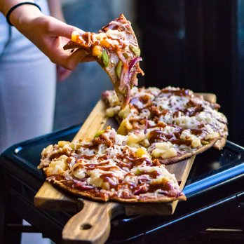 Vegan Cave Cafe - a person taking a slice of pizza - Pizza Near Me - Vancouver, British Columbia