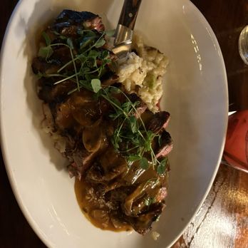 River & Post - New york strip - A dish featuring sliced steak topped with mushroom gravy and microgreens, served with mashed potatoes in a white oval plate. - Lounges Near Me - Jacksonville, Florida