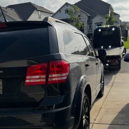 Leander Towing getting my car taken care of - A black SUV is parked in a residential driveway, with a tow truck positioned behind it, indicating vehicle towing or roadside assistance.