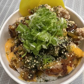 Ichiro - Karaage rice bowl - A rice bowl contains various toppings such as chopped green onions, pickles, and a sauce with sesame seeds. The dish appears to include fried or cooked meat and is garnished with green onions. The bowl is placed on a textured, metallic-looking surface. - Japanese Near Me - Tempe, Arizona