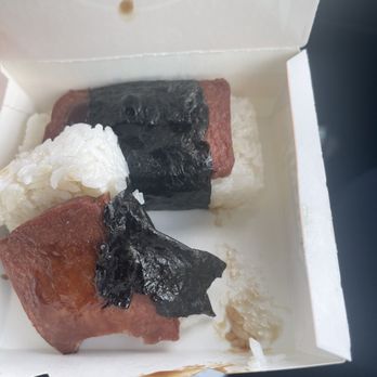Quickly Boba Cafe - Matsubi - A small white takeout container contains two pieces of sushi, each wrapped with seaweed. One piece has rice and fish, and the other has rice, fish, and seaweed. There are some rice grains and sauce remnants at the bottom of the box. - Coffee & Tea Near Me - Saline, Michigan