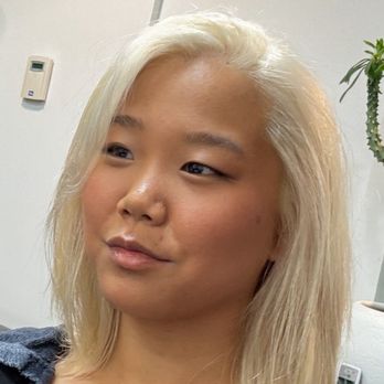 Scott Hair - Color result - A woman with platinum blonde hair and light skin is in an indoor space, possibly an office, with a plain wall and some objects in the background. - Hair Stylists Near Me - Allston , Massachusetts
