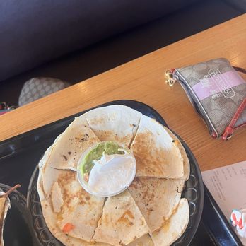 Taco Cabana - Large Quesadillas - A plate of sliced quesadillas served with guacamole and sour cream, placed on a black tray at a restaurant table. - Mexican Near Me - Albuquerque, New Mexico