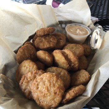 The Maple Leaf Pub - Fried pickles appetizer! Amazing! - Basket of fried pickles with dipping sauce on parchment paper at an outdoor dining area, with a menu and drink in the background. - Bars Near Me - Westfield, Massachusetts