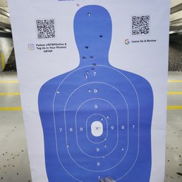 Target Practice - A paper shooting target with bullet holes, featuring a human silhouette and concentric scoring rings, is displayed at an indoor shooting range.