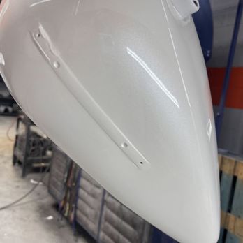 Havana Kustoms - The image shows a white motorcycle fairing with a mounting bracket attached, positioned in a workshop setting. The fairing has a smooth, glossy finish, and the background includes workshop tools and equipment, indicating it is in the process of being repaired or customized. - Body Shops Near Me - Addison, Illinois